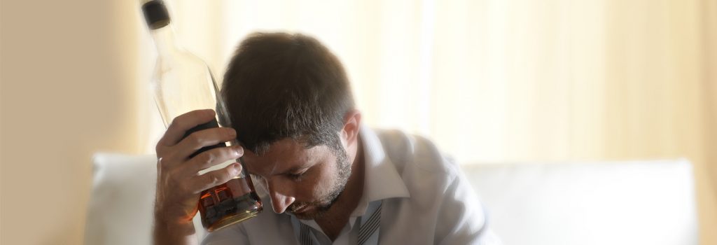 Alcohol Treatment - A man sits alone drinking thinking about getting alcohol treatment for his alcoholism.