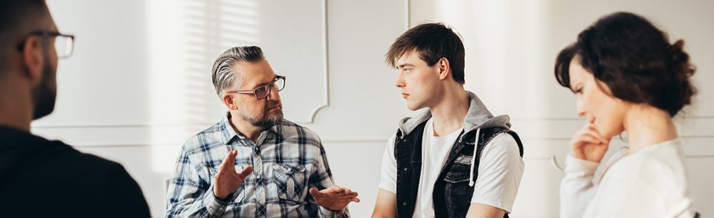Drug Rehab in Colorado  - 3 men and a woman meet for a group therapy session at a drug rehab in Colorado to discuss coping skills to stay sober.