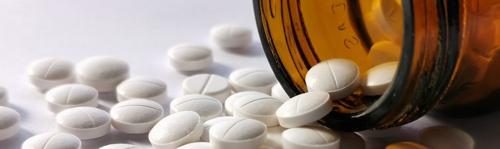 Amphetamine Addiction - A bottle of pills lays on it side with small white amphetamine pills spilling out.