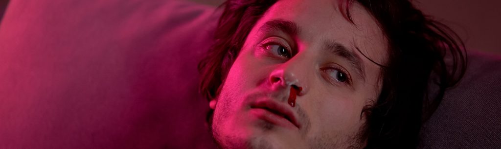 Amphetamine Addiction - A man sits on his couch with a small amount of blood under his nose. This is a sign of amphetamine addiction.