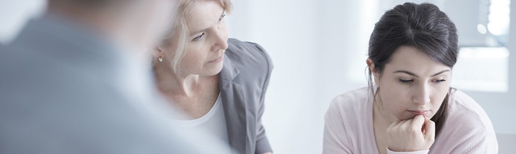 The Continuum of Care - A woman looks down at the floor during her group therapy as her counselor tries to reconnect with her. She is attending a residential addiction treatment program as outlined in the ASAM's Continuum of Care guidelines.